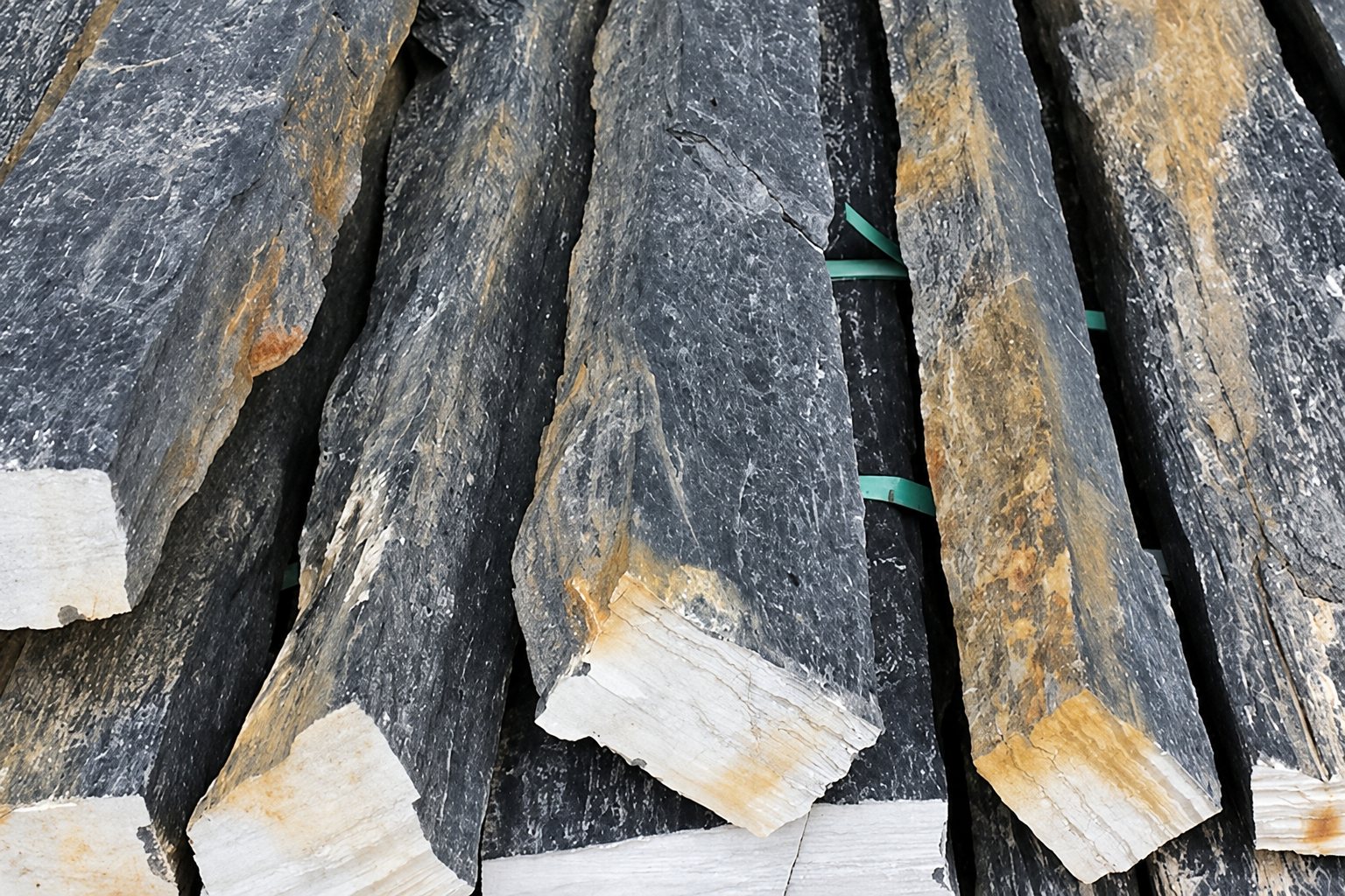 Des blocs allongés de pierre naturelle gris foncé aux extrémités claires sont empilés et maintenus par des sangles vertes.